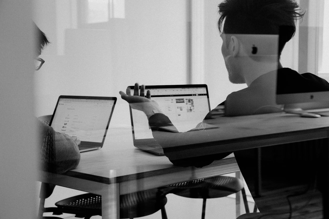Two people working on laptops at a table, in black and white